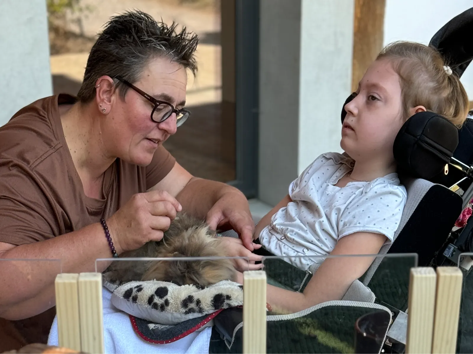 Pflegeperson unterstützt ein Kind beim Streicheln eines Meerschweinchens in der Tiertherapie