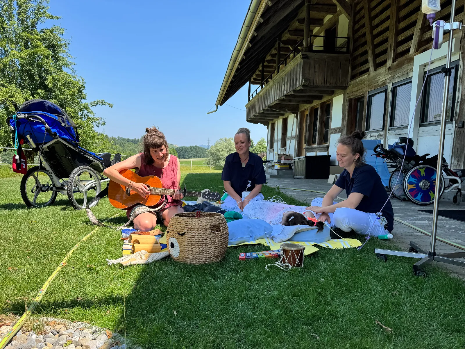 Drei Personen bei einer Musiktherapie im Garten, Gitarre im Einsatz, Kind liegt am Boden