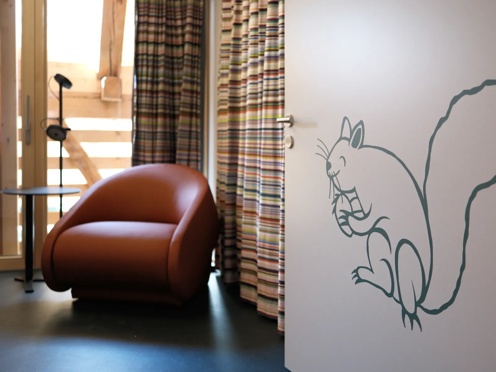 Tür mit Eichhörnchenmotiv und Beschriftung, dahinter steht ein roter Sessel