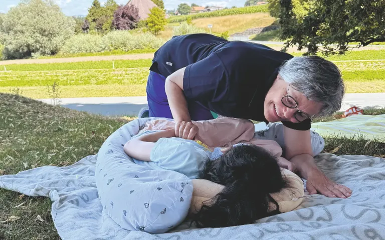 Pflegeperson betreut ein Kind auf einer Wiese im Freien