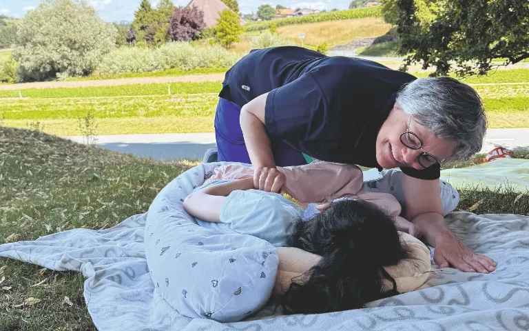 Pflegeperson betreut ein Kind auf einer Wiese im Freien