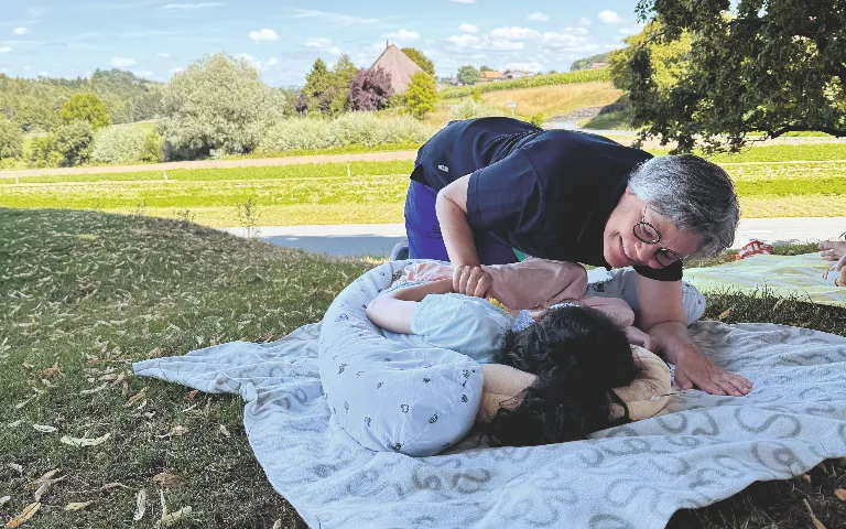 Pflegeperson betreut ein Kind auf einer Wiese im Freien